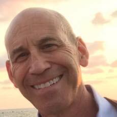 Smiling man with close cropped hair looking at the camera over an orange sunset