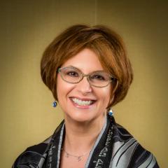 Smiling. Short light brown hair. Glasses. Drop earings, tallit