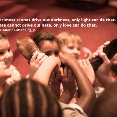 Photo with children touching a shorfar. Quote: Darkness cannot drive out darkness, only light can do that. Hate cannot drive out hate, only love can do that.