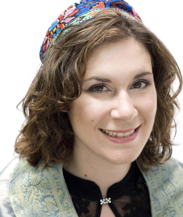 smiling woman with medium length brown hair. wearing a colorful kippah, black shirt and green jacket