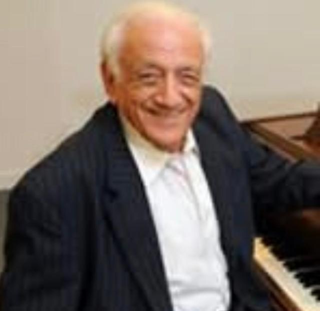 Older gentleman wearing a tuxedo sitting at a piano smiling