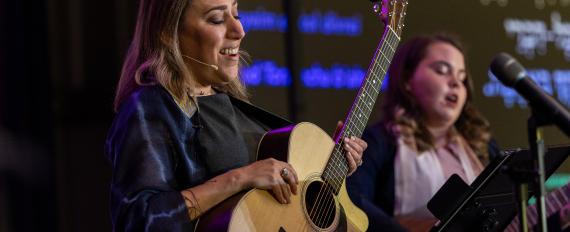 Two women in blue dresses singing and playing guitars